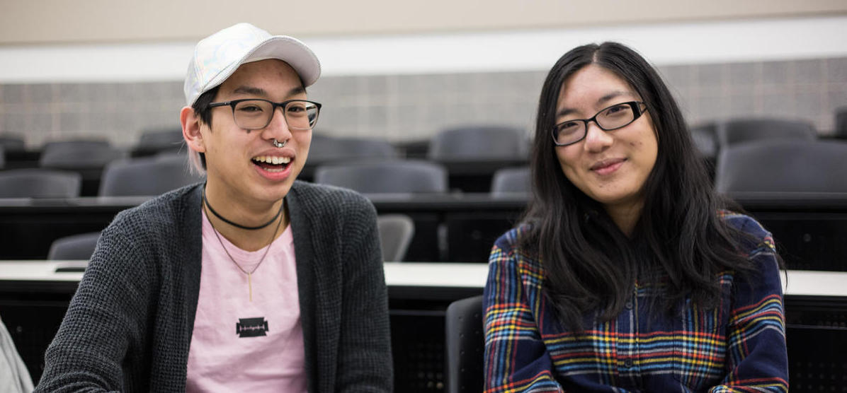 Image of two people sitting in a lecture hall and smiling at the camera. 