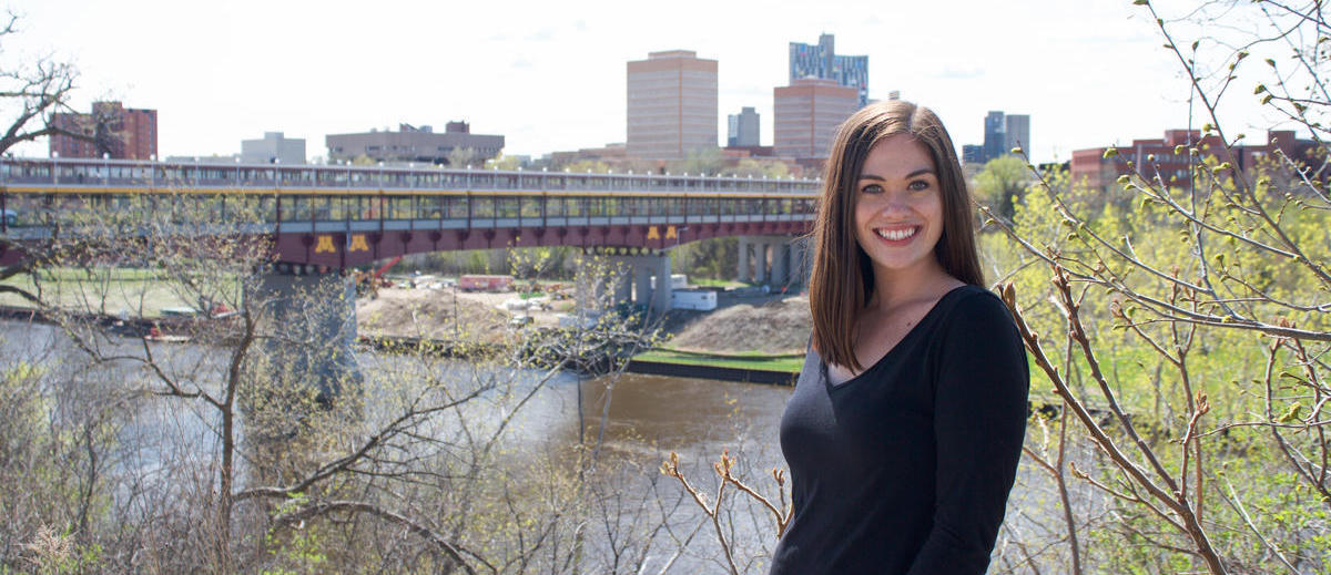 Image of someone outside posing in front of the Washington Avenue Bridge and smiling.