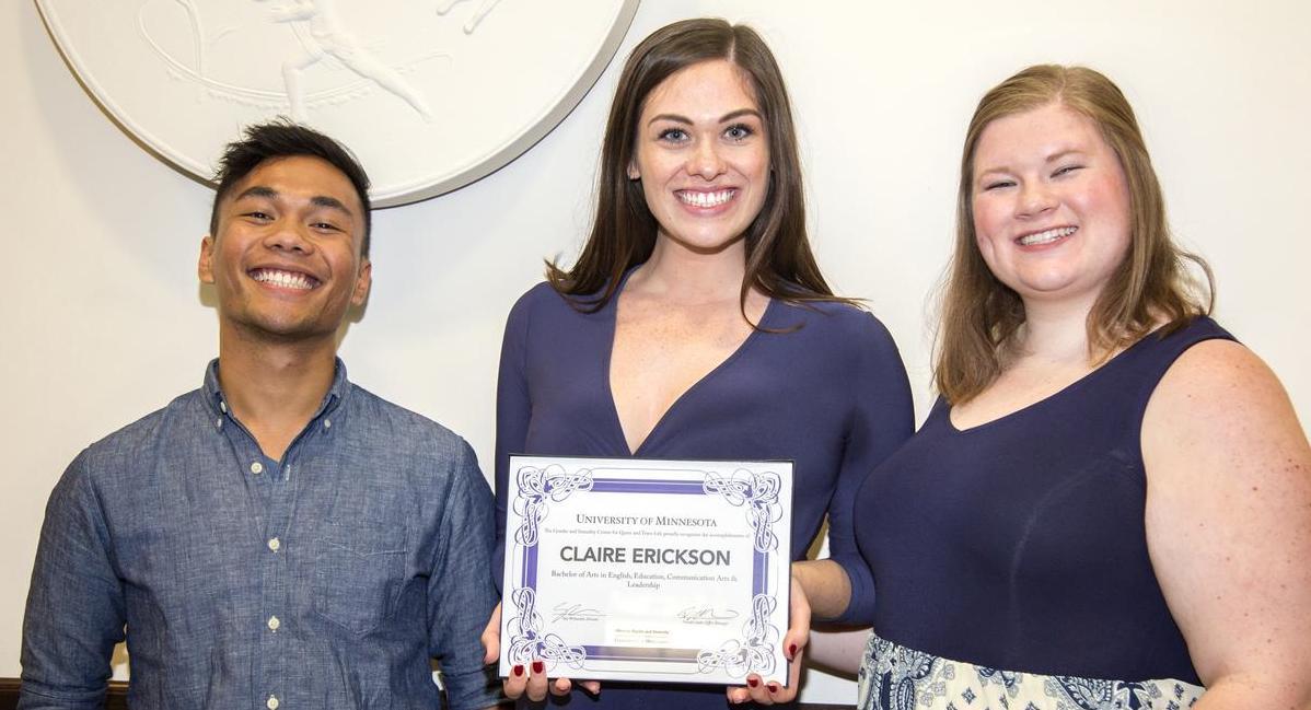 Image of three people standing next to each other and smiling. The middle person is holding a certificate.