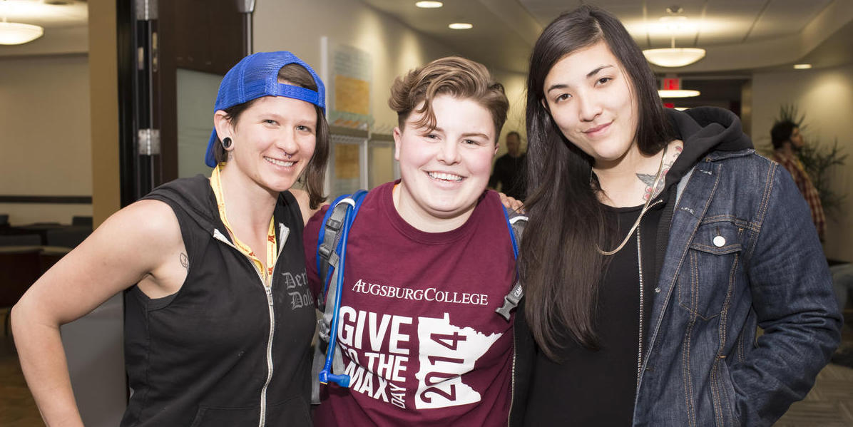 Image of three smiling people standing in a hallway of Coffman Memorial Union with their arms around one another.